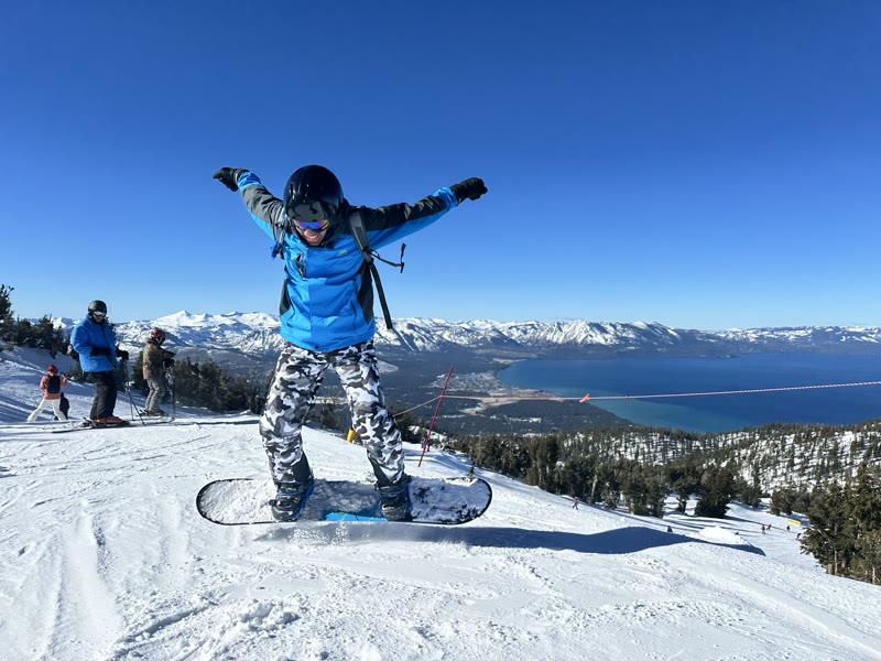 Teja on a snowboard, with a lake and snowy mountains in the distance