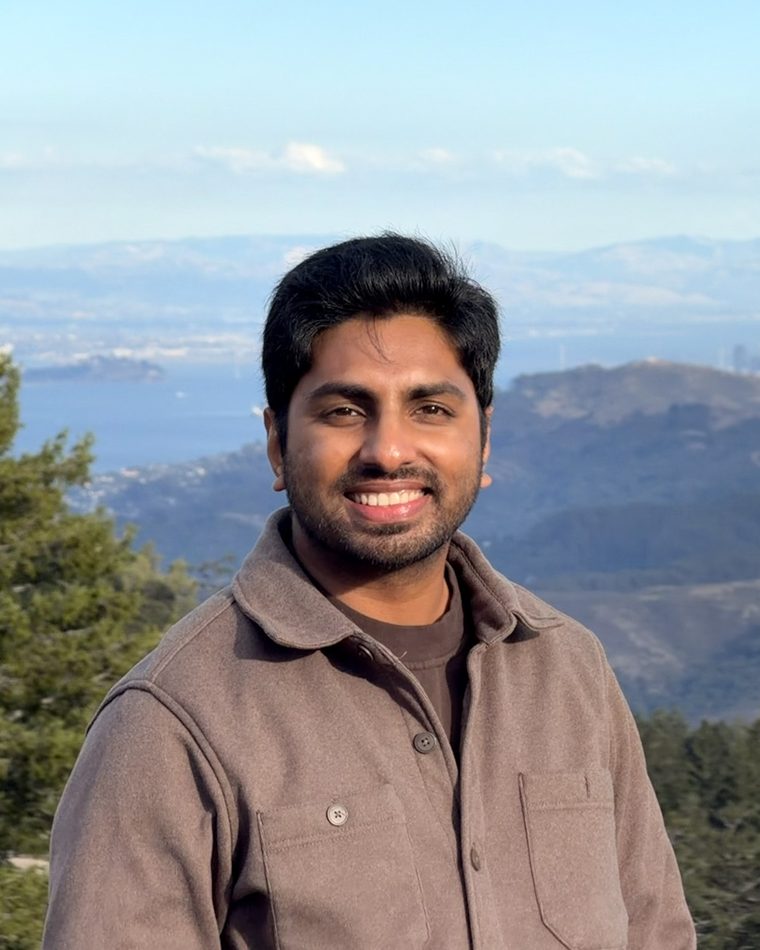 Teja smiling on a hilltop, with the bay and a city skyline behind him